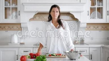 微笑着穿着白色衬衫的年轻女人一边吃纯素沙拉，一边品尝新鲜的有机黄瓜片