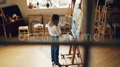 有创造力的年轻女士忙于绘画，独自在现代工作室工作，配备木制家具、画架和艺术工具