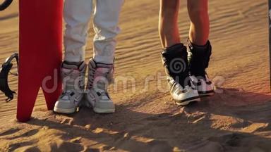 <strong>沙盘</strong>，<strong>沙盘</strong>.. 双脚特写，两个女孩穿着靴子，滑雪板站在沙滩上，准备迎接