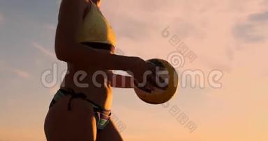 一位身穿比基尼、日落时带球的美女正准备在沙滩排球比赛中发球跳跃