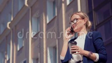 一个嘴唇和眼镜上涂着红色口红的年轻女孩站在阳光明媚的街道上的一栋办公楼附近。 女孩