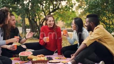 快乐的朋友会说会笑的慢动作，然后在野餐时坐在毯子上品尝和敲打眼镜