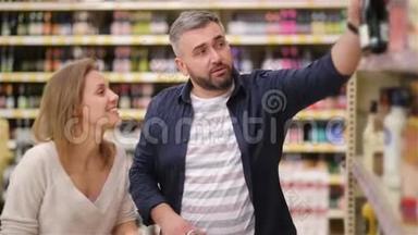 在超市购物快乐情侣。 年轻的家庭从超市货架上挑选葡萄酒。