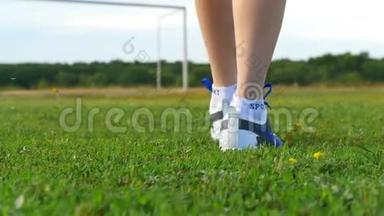 一个长着美丽纤细腿的女孩走在绿色的田野上。 女足穿运动鞋`特写。 体育和户外活动
