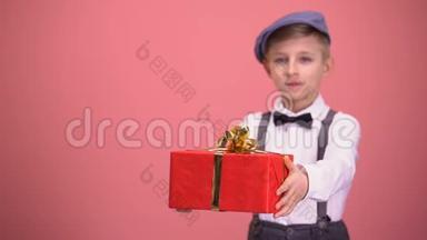 穿着领结和吊带的男孩向相机展示礼品盒，节日礼物