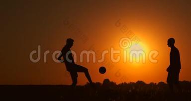 两个男孩在日落时踢足球。 日落时孩子们玩球的<strong>剪影</strong>。 幸福家庭的概念
