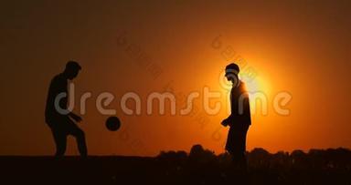 两个男孩在日落时踢足球。 日落时孩子们玩球的<strong>剪影</strong>。 幸福家庭的概念