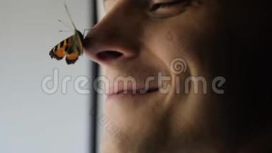 一只美丽的蝴蝶坐在一个年轻人的鼻子上。 那家伙微笑着，蝴蝶<strong>扇动翅膀</strong>。