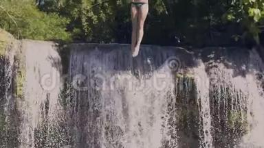 年轻女子从绳子上<strong>跳入</strong>山湖，背景上溅起瀑布。 慢动作。 快乐的女人