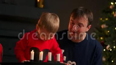 一家人在圣诞节<strong>坐在树下</strong>看着孩子吹灭蜡烛，笑。 妈妈爸爸笑着
