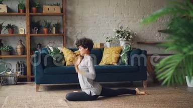 有魅力的年轻女人在家里单独练习时，正在伸展腿和手臂坐在地板上。 健康