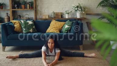 灵活的亚洲女孩正在家里做瑜伽，坐在地板上，独自伸展腿和身体锻炼。 漂亮的房间