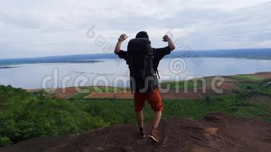 一个快乐的徒步旅行者边上，在一座岩山上举起双臂