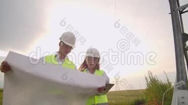 两名电工一起工作，戴着头盔站在输电线路附近的田野里。站在
