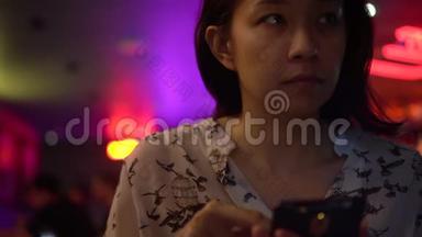 亚洲女人晚上在霓虹灯酒吧打电话