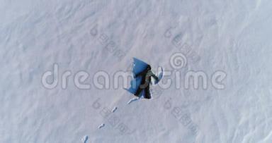 七岁的男孩穿着蓝色夹克做雪天使，空中镜头。 摄像机慢慢地升起