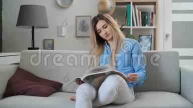 年轻女子在家看杂志。 坐在沙发上看时尚杂志的迷人女孩