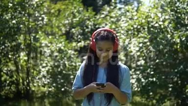 一个长发迷人的女孩走过公园，用耳机听音乐。 慢吞吞的。 高清高清