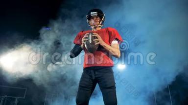 美国足球运动员。 美国足球运动员站在黑暗的多云体育场里带着一个球。
