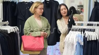 两个年轻的女人穿过商场。 女人购物。 年轻女子在<strong>服装</strong>店挑选<strong>服装</strong>并咨询