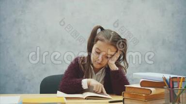 小女孩读一本书坐在灰色的内部。 学习教科书的女学生。 穿校服的孩子