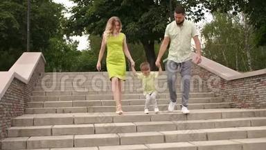 爸爸妈妈和他们的小儿子在公园里走下楼梯，孩子跳了起来。