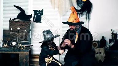 这位穿着巫师服的父亲和他穿着骷髅服的儿子在万圣节的节日里鼓掌。 万圣节
