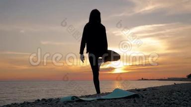 剪影年轻女子在海上<strong>日</strong>落时练习<strong>瑜伽</strong>。 快乐的生活时刻-海滩上的剪影<strong>瑜伽</strong>