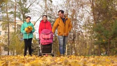 快乐的爸爸妈妈和大孩子沿着秋天的公园散步，带着小宝宝和微笑在婴儿车前滚动