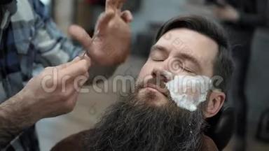 理发师在理发店或理发店用直刃剃须刀刮胡子。 男人`理发和刮胡子