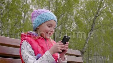 画中的少年女孩在绿树背景的春天公园里用手机