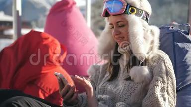 一个女孩用智能手机坐<strong>在滑雪场</strong>的咖啡馆里。 年轻女子<strong>在</strong>高山<strong>滑雪场</strong>放松。