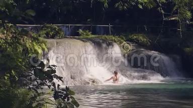 快乐的女人享受来自热带瀑布的流水。 年轻女子在瀑布里洗澡，流水潺潺