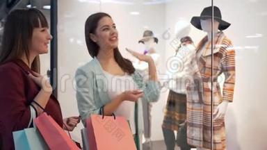 购物周末，商店橱窗附近的时尚女孩在昂贵的商店里讨论时尚的服装