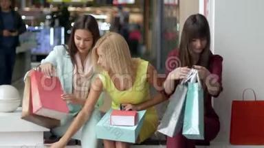 穿着五颜六色衣服的女朋友在购物后一起讨论他们的购买，而坐在购物中心的黑色