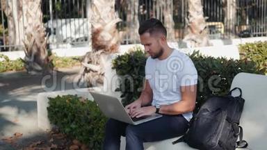 微笑的年轻人在笔记本电脑上工作，坐在长凳上，拿着<strong>旅行箱</strong>和包，背包游客在度假