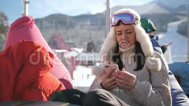 在高山滑雪场放松的年轻女子。一个女孩坐在滑雪场的咖啡馆里用智能手机。