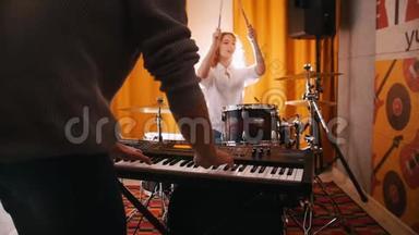 重复。 男人在键盘上玩，女孩在后台<strong>打鼓</strong>。 背光灯。 把注意力集中在手上。 从男人的背后看