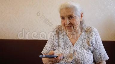 老妇人用遥控器和微笑切换电视频道。 奶奶`在看电视。