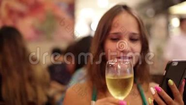 年轻的美女在咖啡馆喝葡萄<strong>酒</strong>，并使用手机在bokeh灯的背景。 1920x1080