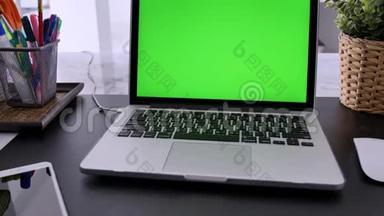 在客厅的办公桌上展示绿色彩色钥匙屏幕的笔记本电脑。 在背景舒适的客厅里。 倾斜向下