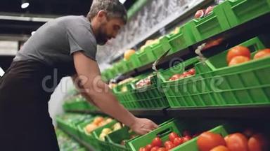 穿着制服的强有力的推销员带着塑料盒子，在超市里放水果和水果。