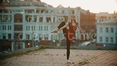 年轻女子芭蕾舞演员在屋顶上训练-站在展示她伸展的姿势-日落