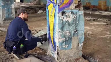 现代涂鸦画家蹲在旧废弃建筑的柱子附近，用喷漆涂鸦
