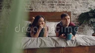 年轻人正在看电视，他的女朋友躺在床上<strong>拿</strong>着<strong>遥控</strong>器，他们<strong>拿</strong>着枕头和杯子