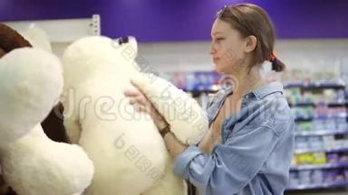 快乐，积极，微笑的女人买家从超市<strong>货架</strong>上选择<strong>玩具</strong>。 一只白色柔软的大熊