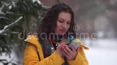 在公园玩滚雪球的时候，一个棕色卷发的女人。 那个女孩拿到雪球时拿着手机。 冬季运动会