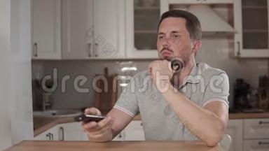 一个胆小的男人正在换电视频道，用遥控器，坐在厨房里