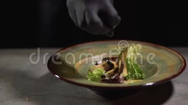 双手戴<strong>黑色食品</strong>手套，将沙拉放在盘子上，放在桌面上，隔离在<strong>黑色</strong>背景上。 <strong>食品</strong>准备