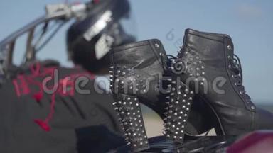 带高跟鞋和黑色和红色连衣裙的加钉鞋躺在摩托车特写上。 戴着头盔的摩托车